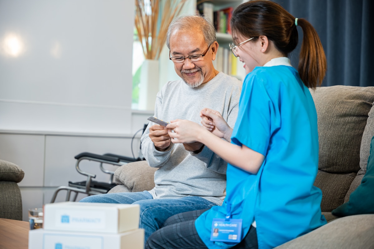 Asian nurse with physician explaining prescription medicine to attentive senior man at home, Doctor woman explain dosage pill old man, Healthcare worker caregiver visiting in house in living room